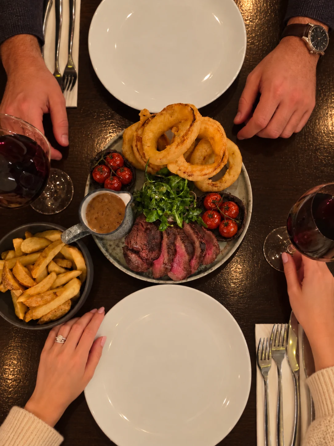 Chateaubriand sharing platter with onion rings, chips, roast tomatoes and red wine on a dark dining table