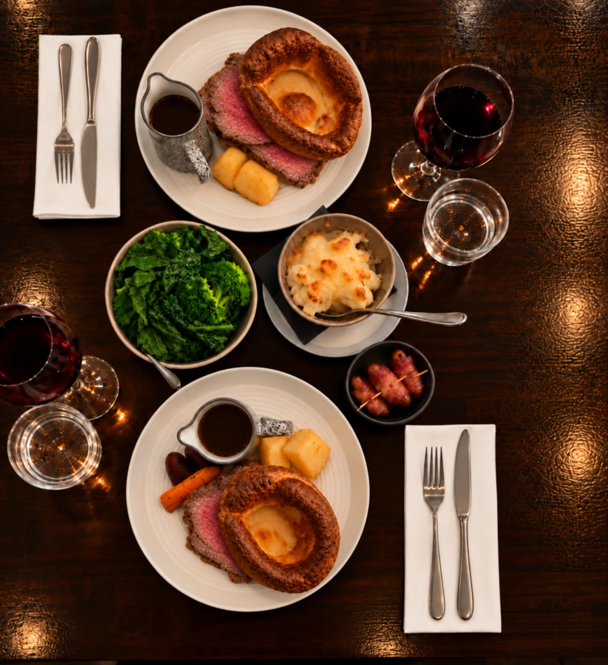 Sunday roast dinner for two with Yorkshire puddings, roast potatoes, green vegetables and gravy on a dark wooden table
